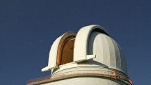 Stars shine in an inky night sky above the open dome of the Harlan J. Smith Tele
