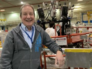 Scientist posing in front of a complex-looking instrument.